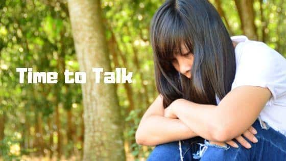 A person sits with head down and arms crossed in a wooded area. Text reads: "Time to Talk."